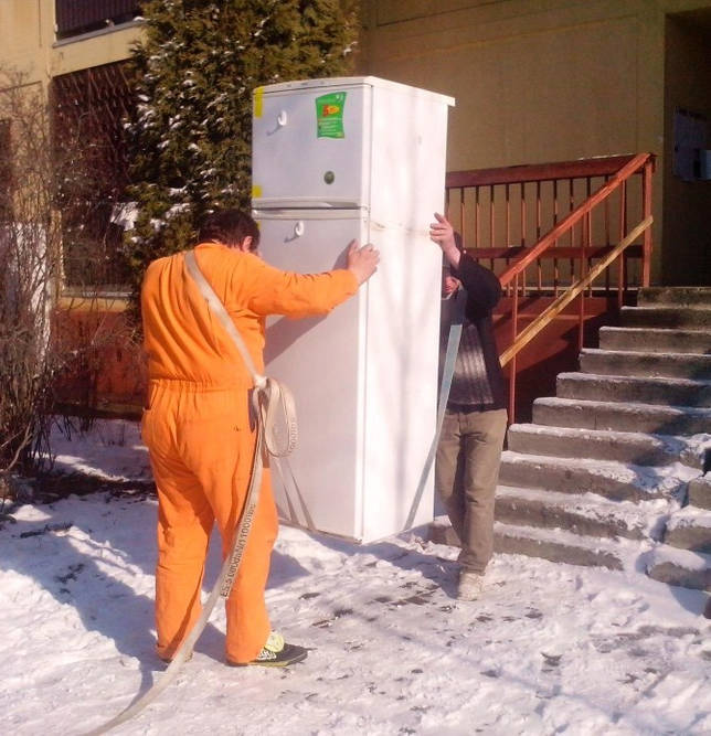 Двое мужчин производят транспортировку бытового холодильника с использованием наплечных ремней